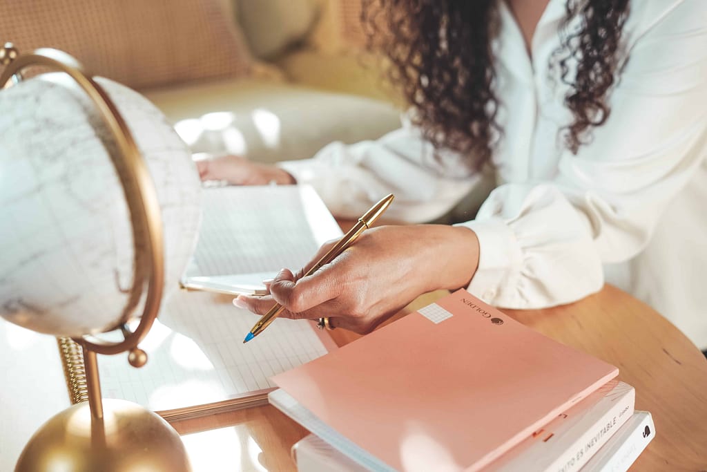Manos escribiendo en un cuaderno de journaling — práctica de autoconocimiento para sanar la relación con el dinero en el curso Emprendedora Abundante.